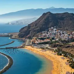 Vista aérea de una playa dorada y un pueblo costero con casas blancas y coloridas en la costa blanca España. Montañas y el mar azul completan la escena.