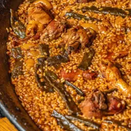 Paella valenciana recién hecha, con trozos de pollo, judías verdes y arroz dorado en una paellera.