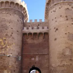 Las **Torres de Quart**, imponentes y con cicatrices históricas, se alzan contra el cielo azul.