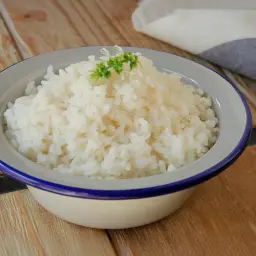Un cuenco de arroz blanco recién cocido, adornado con una ramita verde, descansa sobre una mesa de madera rústica.