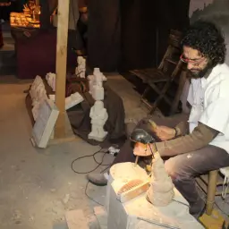 Artesano trabajando en el mascarell mercado medieval, esculpiendo figuras de piedra.