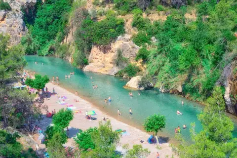Gente disfrutando del sol y el agua cristalina en el balneario de Montanejos, rodeado de exuberante vegetación y rocas.