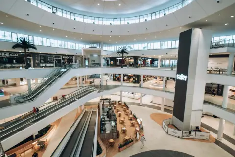Interior de un moderno centro comercial en Valencia, con escaleras mecánicas, palmeras y tiendas. Un lugar ideal para ir de compras.