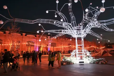 Árbol de luces gigante ilumina el parque central Valencia Navidad. Gente pasea bajo luces cálidas y una estructura moderna.