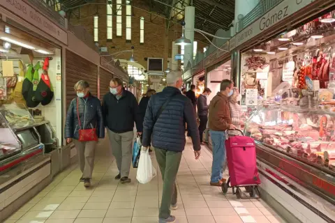 Gente comprando en el mercat central d'Alacant, con puestos de embutidos y carnes.