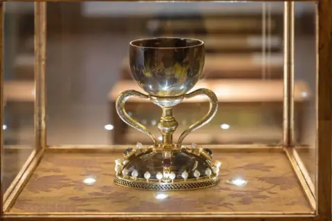 Cáliz dorado con asas, adornado con perlas y gemas, exhibido en vitrina. ¿Será este donde está el santo grial?
