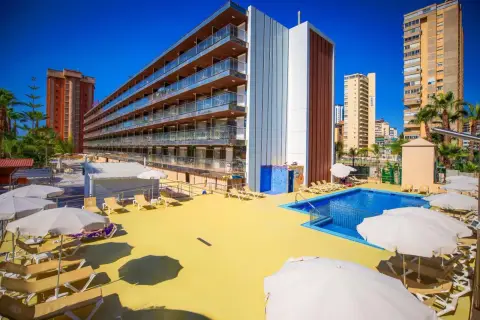 Terraza soleada con piscina y tumbonas en el hotel Diplomatic Benidorm. Edificio moderno con balcones y palmeras.