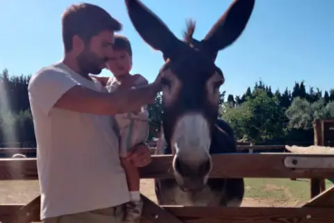 Un padre y su hijo visitan un burro en la granja escola corral de neri.