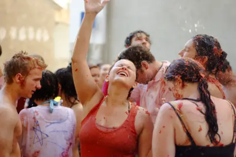 Gente feliz y empapada de tomate en la Tomatina, con una mujer riendo a carcajadas y el brazo en alto.