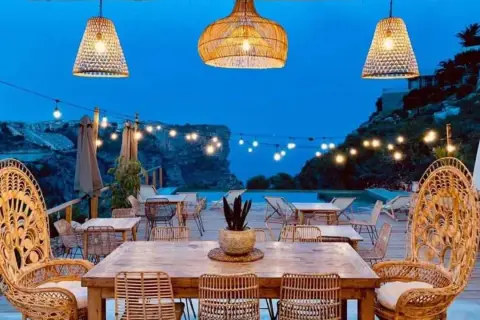 Un rincón de ensueño en el **dreamsea mediterranean camp**. Mesas de madera, sillas de ratán y luces cálidas bajo un cielo estrellado.