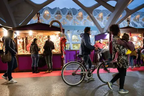 Gente pasea por puestos del **Valencia Christmas Market** bajo una estructura futurista.