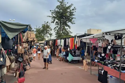 Gente paseando por el mercadillo de Canet de Berenguer, viendo bolsos, ropa y lencería expuestos en puestos.