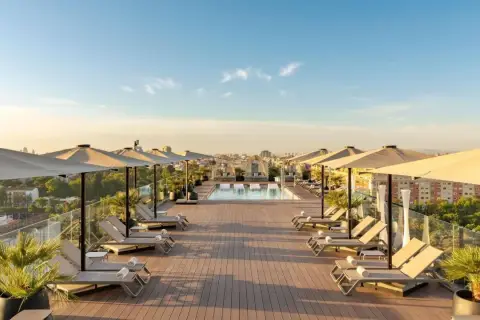 Terraza con piscina y tumbonas en el Novotel Valencia, vistas a la ciudad al atardecer.