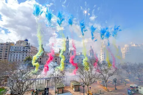 Explosión de color y ruido en la mascletà hoy. El cielo se tiñe de azul, amarillo y rosa sobre edificios históricos.