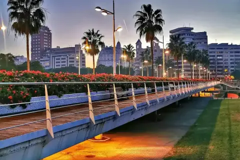 Puente iluminado con palmeras y flores rojas en la ciutat vella valencia al atardecer.