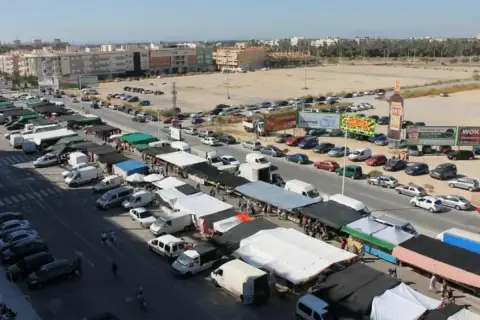 Vista aérea de un bullicioso mercadillo en Elche, con puestos, furgonetas y coches aparcados.