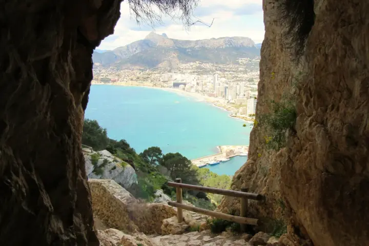 Vista desde la ruta peñón de ifach: mar turquesa, ciudad costera y montañas.