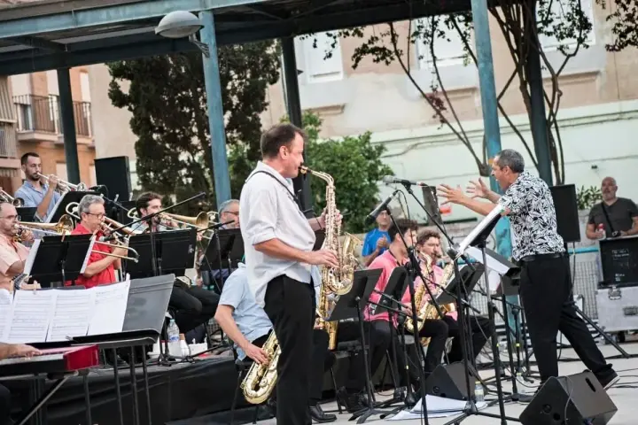Saxofonista toca en concierto de jazz en Valencia. La banda de metales suena con energía bajo un toldo.
