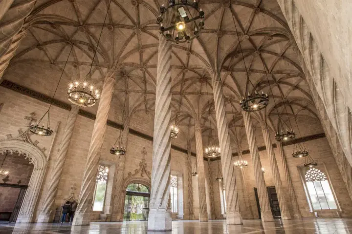 Interior de la lonja de la seda, con sus icónicas columnas helicoidales y bóvedas góticas, iluminado por candelabros.