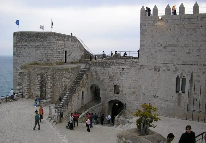 El castillo del Papa Luna en Peñíscola, con sus murallas de piedra y escalinatas, recibe a visitantes que pasean por sus patios.
