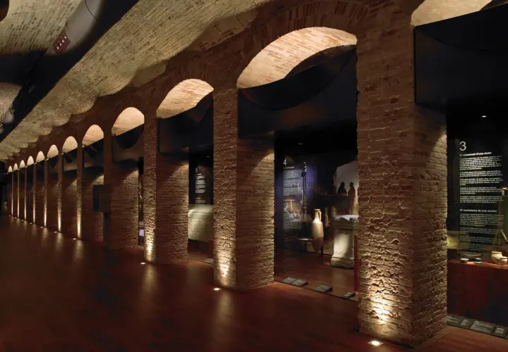 Pasillo del museo de historia de Valencia, con arcos de ladrillo, iluminación tenue y vitrinas con artefactos antiguos.