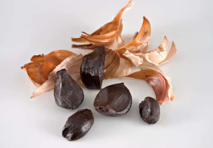 Dientes de ajo negro, con cáscaras secas de color naranja y blanco, evocan el sabor único del ajo negro alicante.