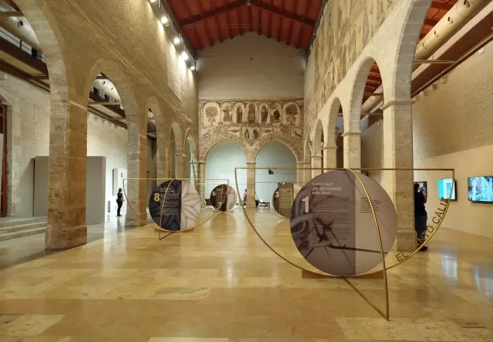 Exposición en el Almudín de Valencia, con arcos de piedra, murales antiguos y paneles circulares que narran la historia del Santo Cáliz.