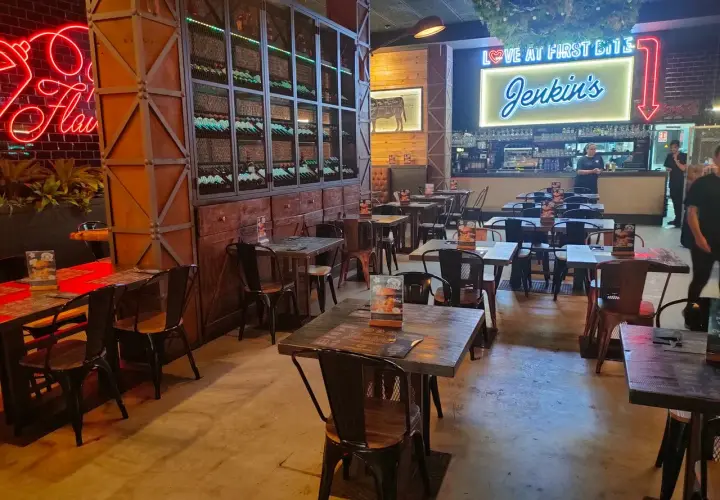 Interior de Jenkins Valencia, un restaurante con mesas de madera, sillas metálicas y un letrero de neón que dice "Love at First Bite Jenkins".