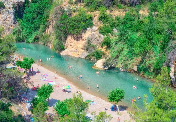 Gente disfrutando del sol y el agua cristalina en el balneario de Montanejos, rodeado de exuberante vegetación y rocas.