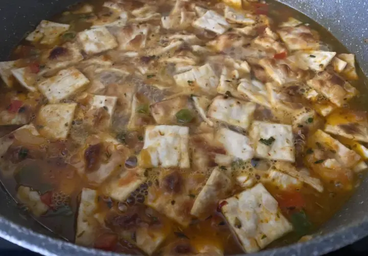Gazpacho marinero alicantino burbujeante en una sartén, con trozos de pan tostado y verduras.