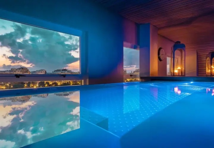 Piscina iluminada con luces azules en un spa de Valencia, con vistas a la ciudad al atardecer.