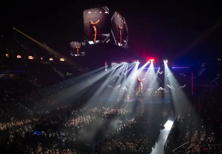 Un artista en un escenario iluminado por focos, con pantallas gigantes mostrando su imagen. ¡Imagina los conciertos Valencia 2026!