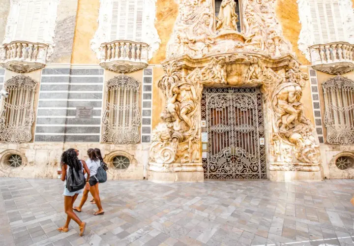 Dos chicas pasean frente a un edificio ornamentado, buscando museos gratis en Valencia.
