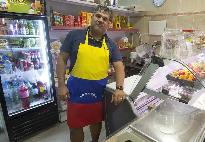 Hombre con delantal de Venezuela en el mercado de Torrefiel, rodeado de productos en neveras y estanterías.