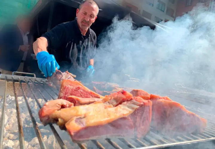 Hombre con guantes azules cocina carne en una parrilla humeante, un festín de carne en el **meat carnival Valencia**.
