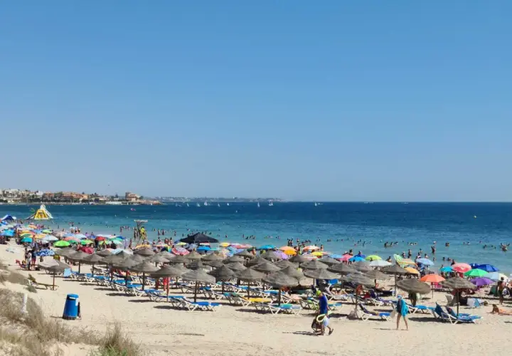 Día soleado en la playa de las Higuericas, con mucha gente disfrutando del mar y la arena bajo coloridas sombrillas.