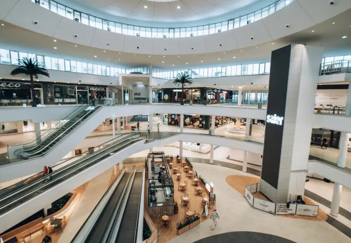 Interior de un moderno centro comercial en Valencia, con escaleras mecánicas, palmeras y tiendas. Un lugar ideal para ir de compras.