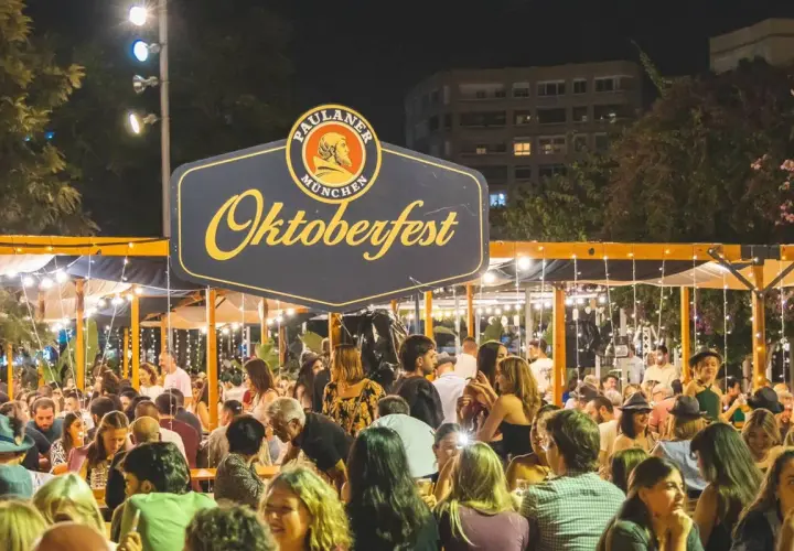 Gente disfrutando en un evento de Oktoberfest Valencia, con luces y un gran cartel de Paulaner.
