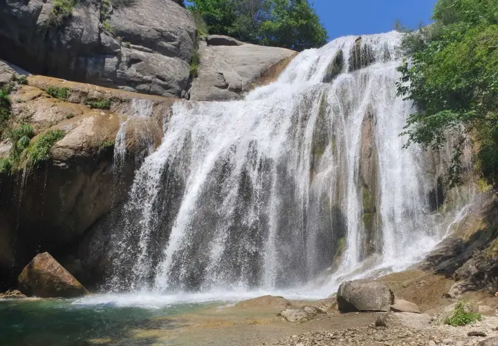 Cascada del Moli, con agua cayendo sobre rocas y vegetación exuberante, formando una piscina natural.