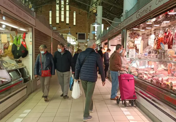 Gente comprando en el mercat central d'Alacant, con puestos de embutidos y carnes.