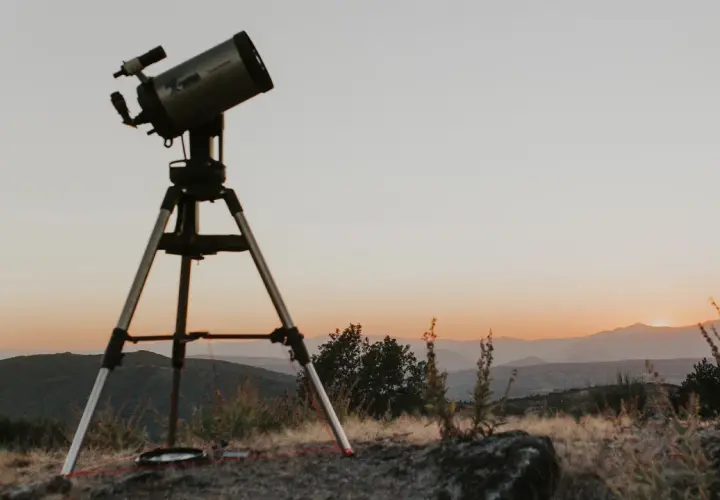 Telescopi preparat per a un sopar amb estrelles. El cel s'enfosqueix sobre les muntanyes, prometent una nit d'observació celestial.