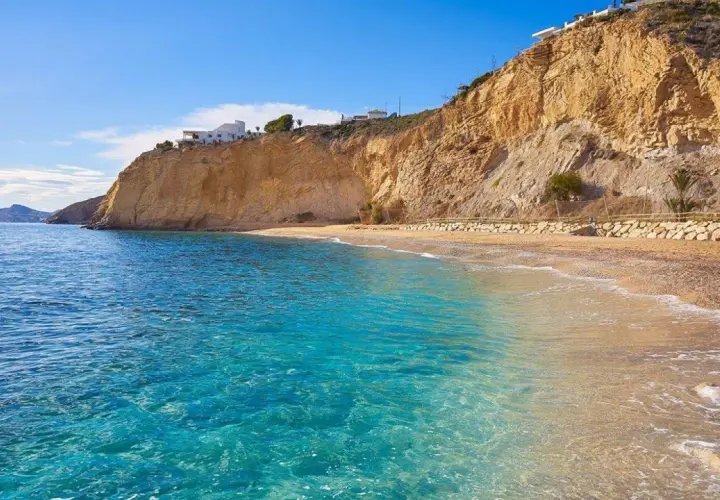 Aguas cristalinas y playas tranquilas en Alicante, con acantilados dorados y casas blancas en la cima.