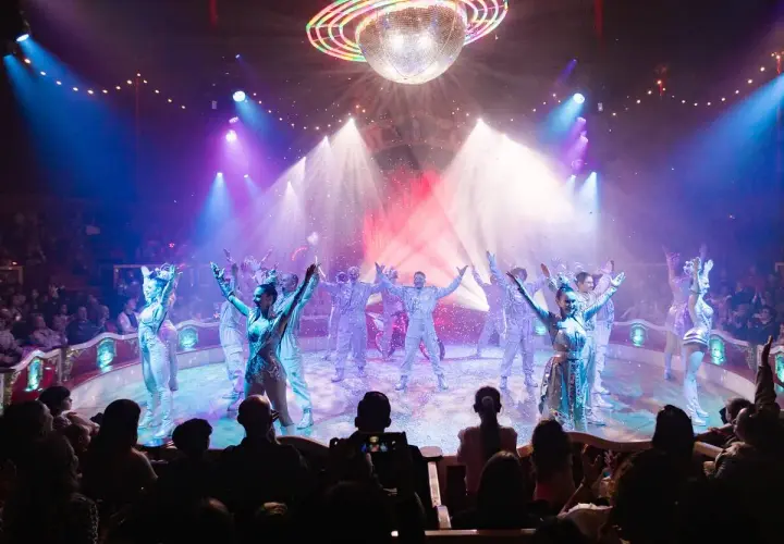 Artistas del circo Raluy en Alicante, bajo una bola de discoteca, con confeti cayendo y público aplaudiendo.