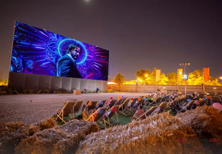 Noche de cine al aire libre en Valencia. Gente relajada en tumbonas viendo una película en pantalla gigante.