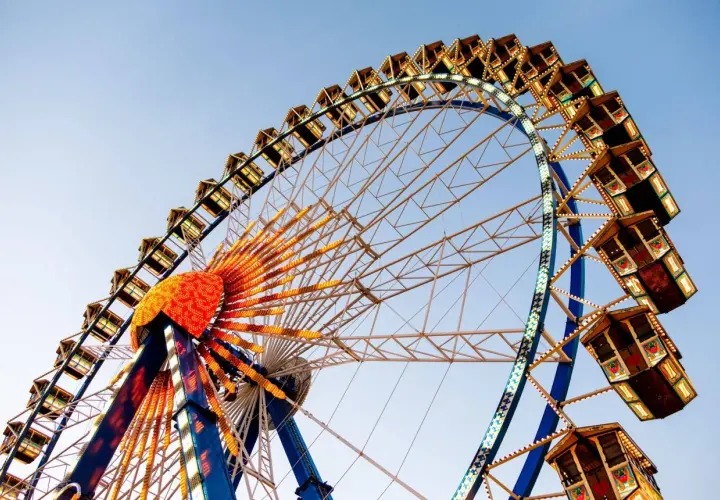 La noria iluminada, una de las atracciones principales de la feria de Valencia, se alza contra el cielo azul.