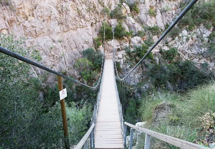 Puentes colgantes de Chulilla, un camino de madera suspendido sobre un barranco rocoso, rodeado de vegetación.