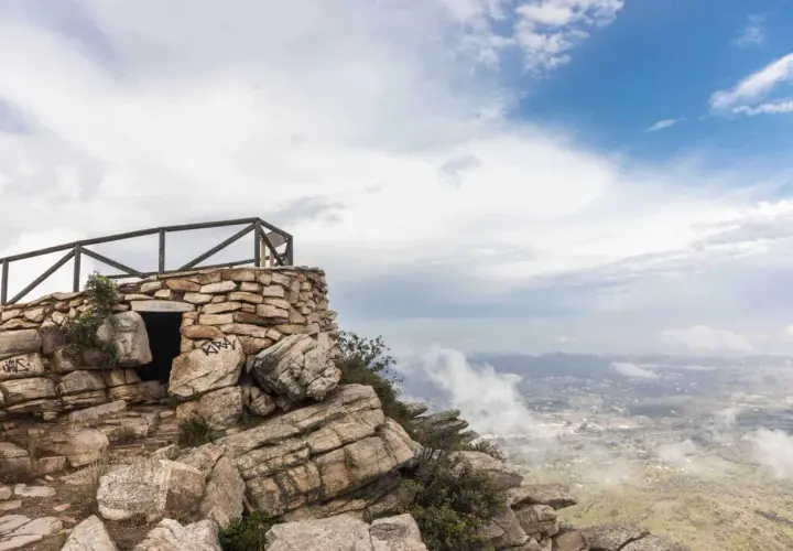 Pequeña construcción de piedra en la cima de una montaña, con barandilla de madera y vistas al valle. El garbí sopla suavemente.