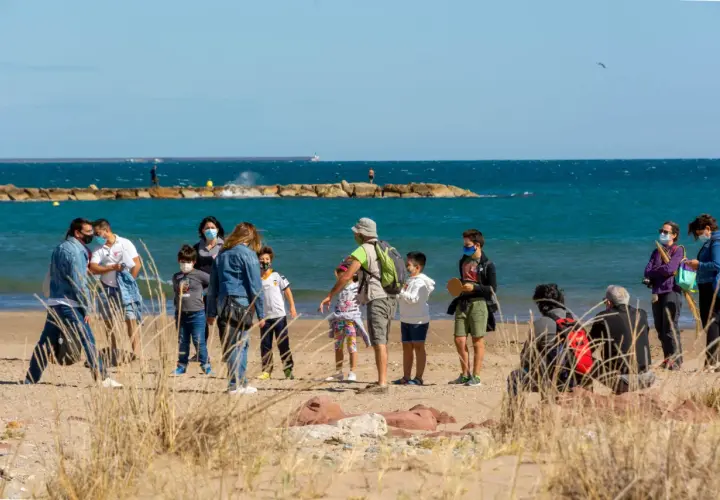 Familias disfrutan de un día soleado en la playa del Puig, con niños jugando y adultos conversando cerca del mar.