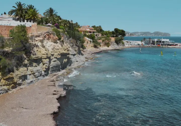 Acantilados y calas rocosas con aguas turquesas, perfectas para descubrir las playas cerca de Calpe. Windsurfistas disfrutan del mar.