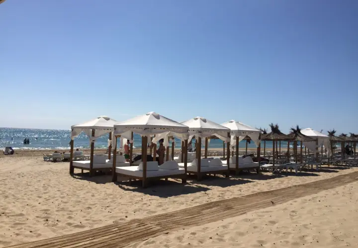 Días soleados en la playa Carabassi, con toldos blancos y camas de día listas para el relax junto al mar azul.